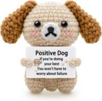 A grey crochet dog miniature figure with floppy ears and blush details, holding a sign with an encouraging message.