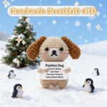 A grey crochet dog miniature figure with floppy ears and blush details, holding a sign with an encouraging message.