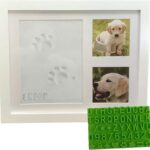White wooden picture frame with a clay paw print impression and two photo slots, with a stencil kit beside it.