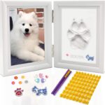 A white rectangular wooden frame with a pet's paw print impression in clay, a photo slot, and decorative trinkets.