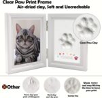 A white rectangular wooden frame with a pet's paw print impression in clay, a photo slot, and decorative trinkets.