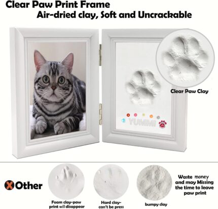 A white rectangular wooden frame with a pet's paw print impression in clay, a photo slot, and decorative trinkets.