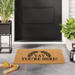 A colorful rectangular doormat with the humorous text "Yay You're Here!" in bold letters, set against a bright background.